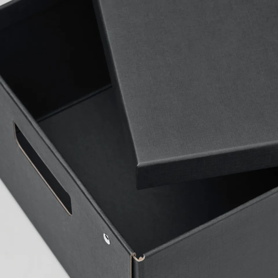 Black storage box with lid slightly open, featuring cut-out handles. Sturdy paper material, neat and organised appearance.