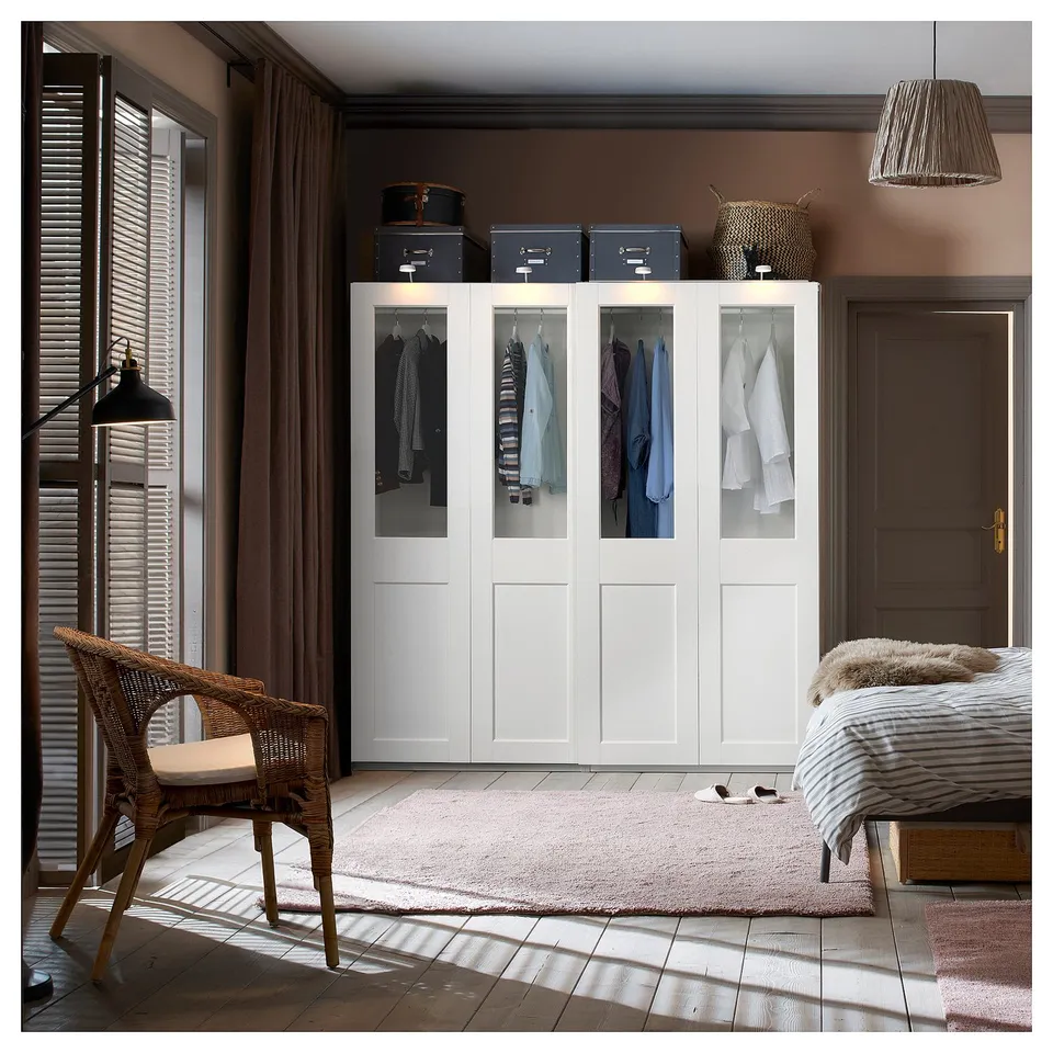 Bedroom with white PAX wardrobe, wicker chair, bed with striped blanket, and large window with curtains.
