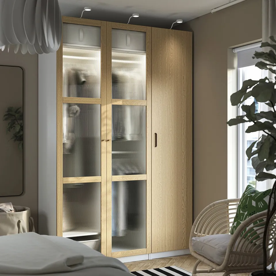 Modern bedroom with TONSTAD wardrobe, glass, and oak veneer. Tall wardrobe, wicker chair with green cushions, ambient lighting.