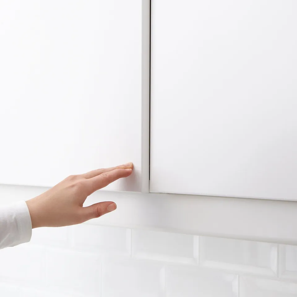 Image shows a hand gently pushing a kitchen cabinet door, opening it without a handle using UTRUSTAs push-to-open mechanism.