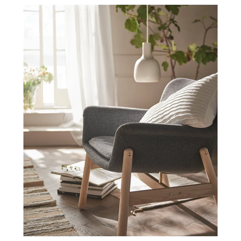 Cosy grey VEDBO chair by window, wooden legs, soft lines, pillows, books, plant.