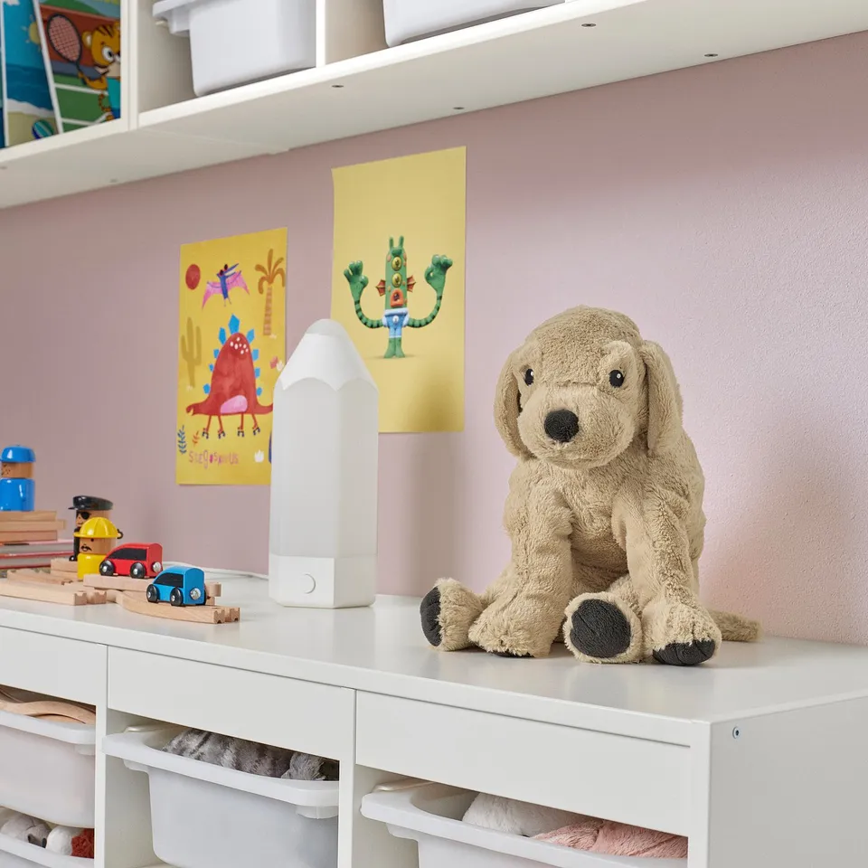 Beige teddy bear gosig on shelf with toys, larger than others.