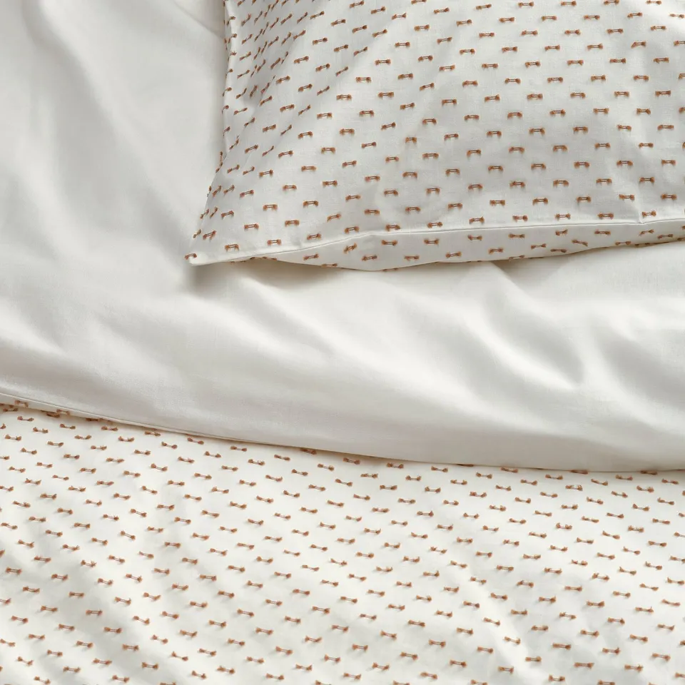 Neatly made bed with white duvet, beige patterns, matching pillow.