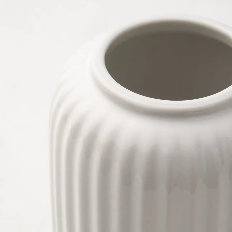 Close-up of a white textured vase with vertical grooves. Top is slightly off-center, sharp and unused.