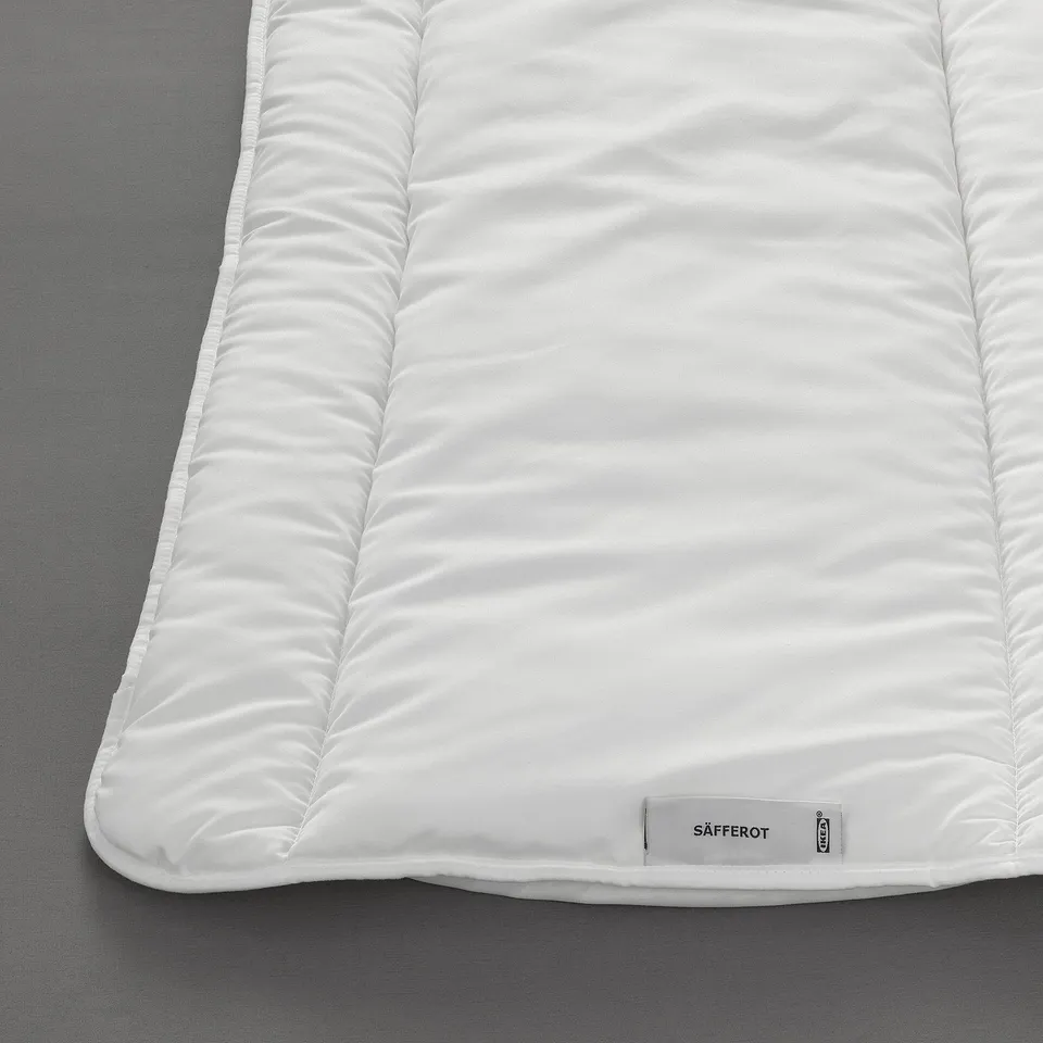A close-up a soft, white SÄFFEROT duvet on a grey surface, showcasing its smooth texture and clean design.