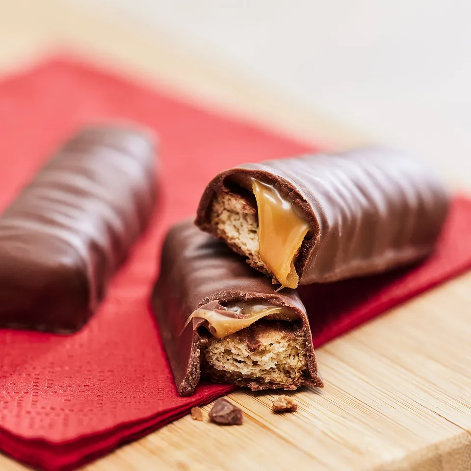Two chocolate bars on red tissue. One is bitten, revealing crispy, chewy caramel and smooth chocolate.