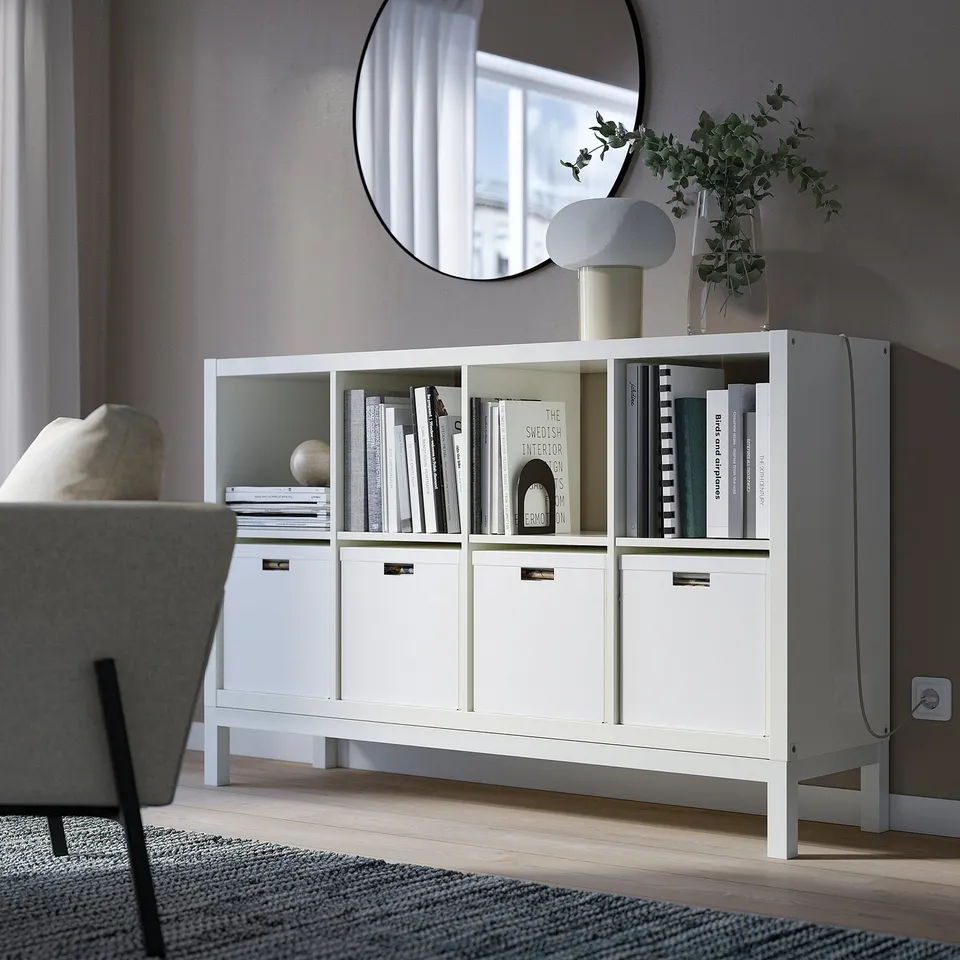 White KALLAX shelf with books & decor near sofa, visible base