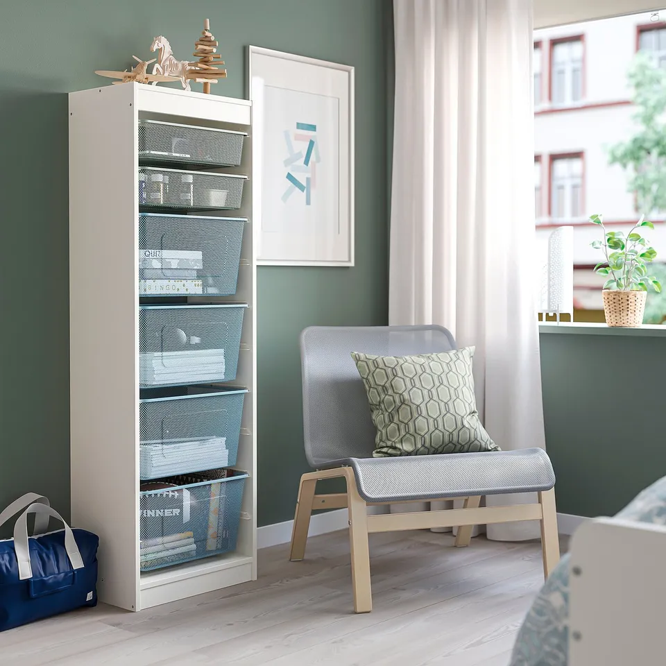 White TROFAST storage unit with mesh baskets, blue bags, and grey cushioned bench by window.