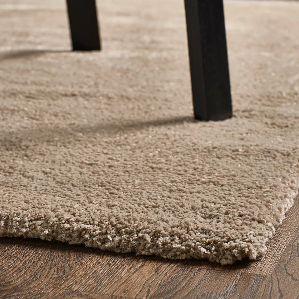 Light grey, plush rug with thick pile on wooden floor, providing comfort and sound dampening.