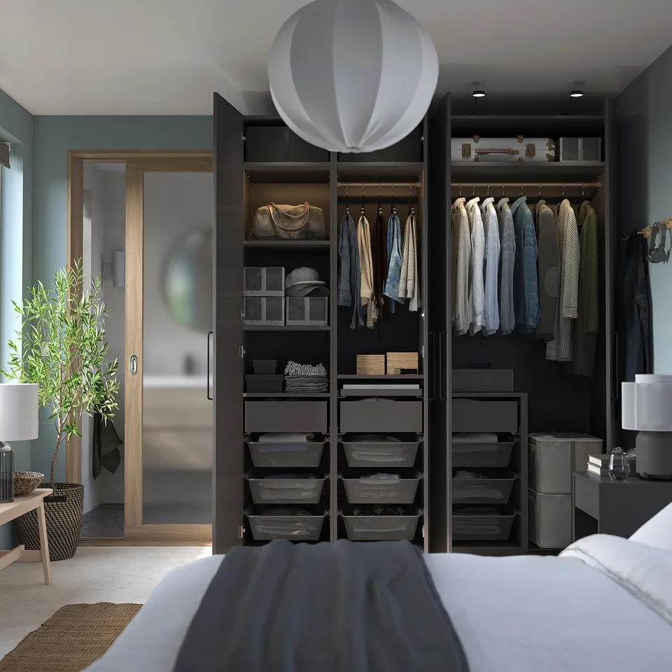 Modern bedroom with black PAX wardrobe, hanging clothes, shelves, and grey organisers. Soft led lighting, hanging lampshade, and a white bed.