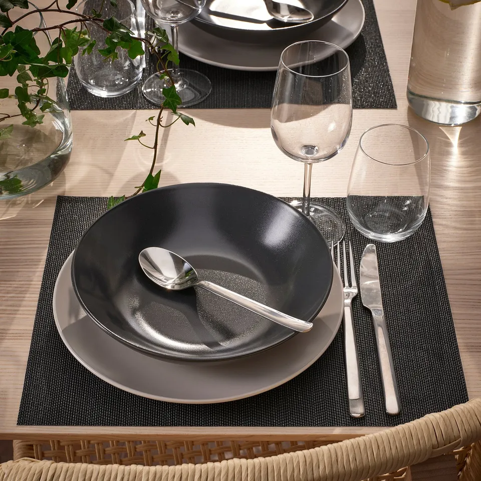 Table set with FLYGFISK place mats, black and grey dishes, cutlery, and glasses.