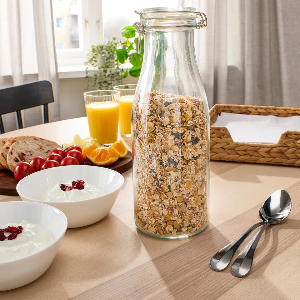 Breakfast table with KORKEN jar of granola, bowls of yoghurt, glasses of orange juice, and spoons.