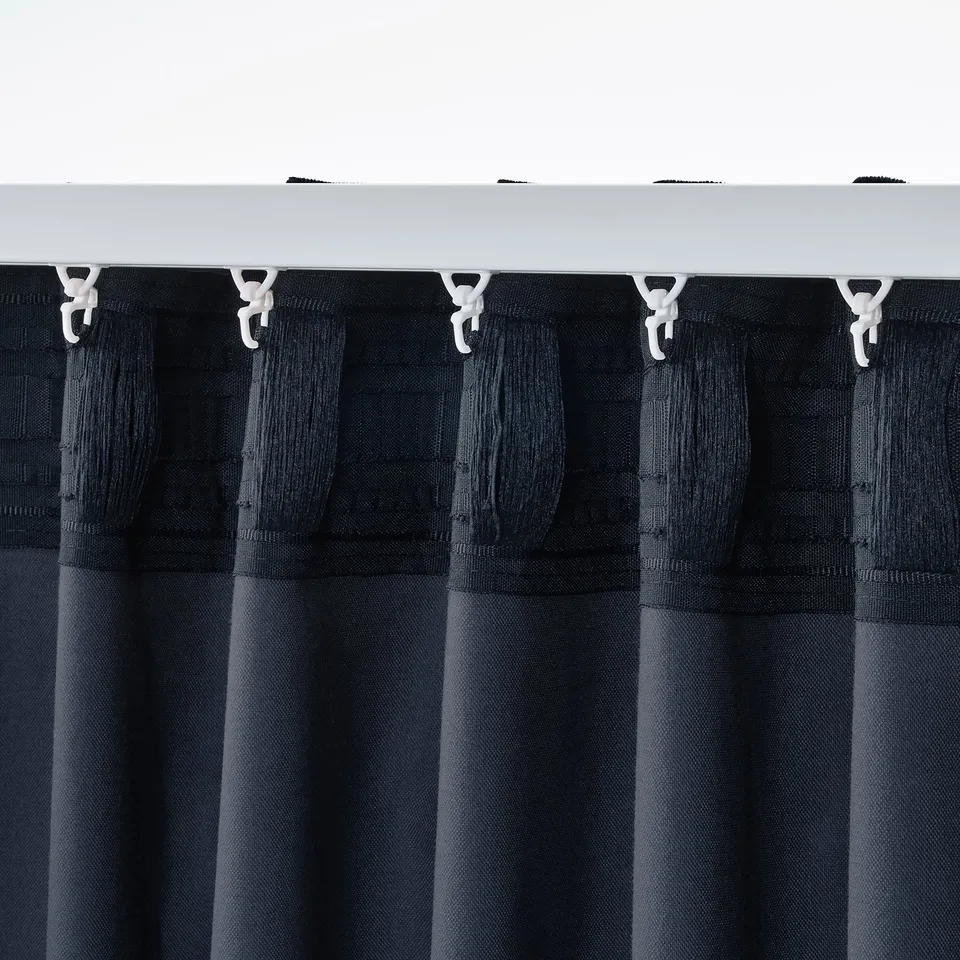 Close-up of black curtains hanging with hooks on a rod, showcasing their pleated design and velvet texture.