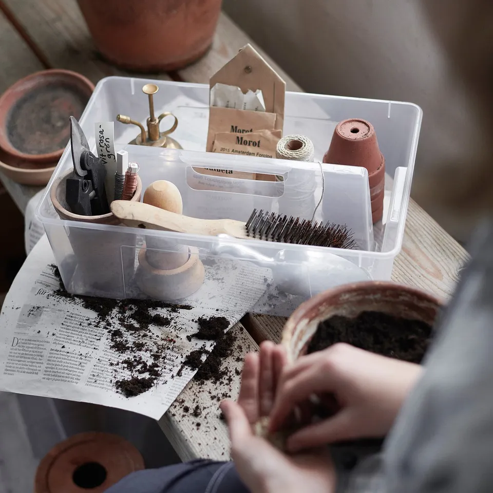 Clear plastic storage box, labelled SAMLA, containing various gardening tools and supplies, including scissors, string, and brushes.