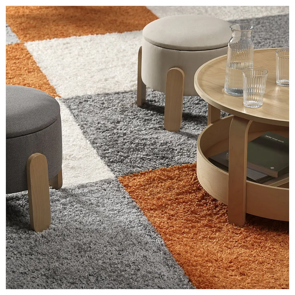 A cosy room setup with an orange ÄRENDE rug, round stools, and a coffee table. The rug multicoloured sections.