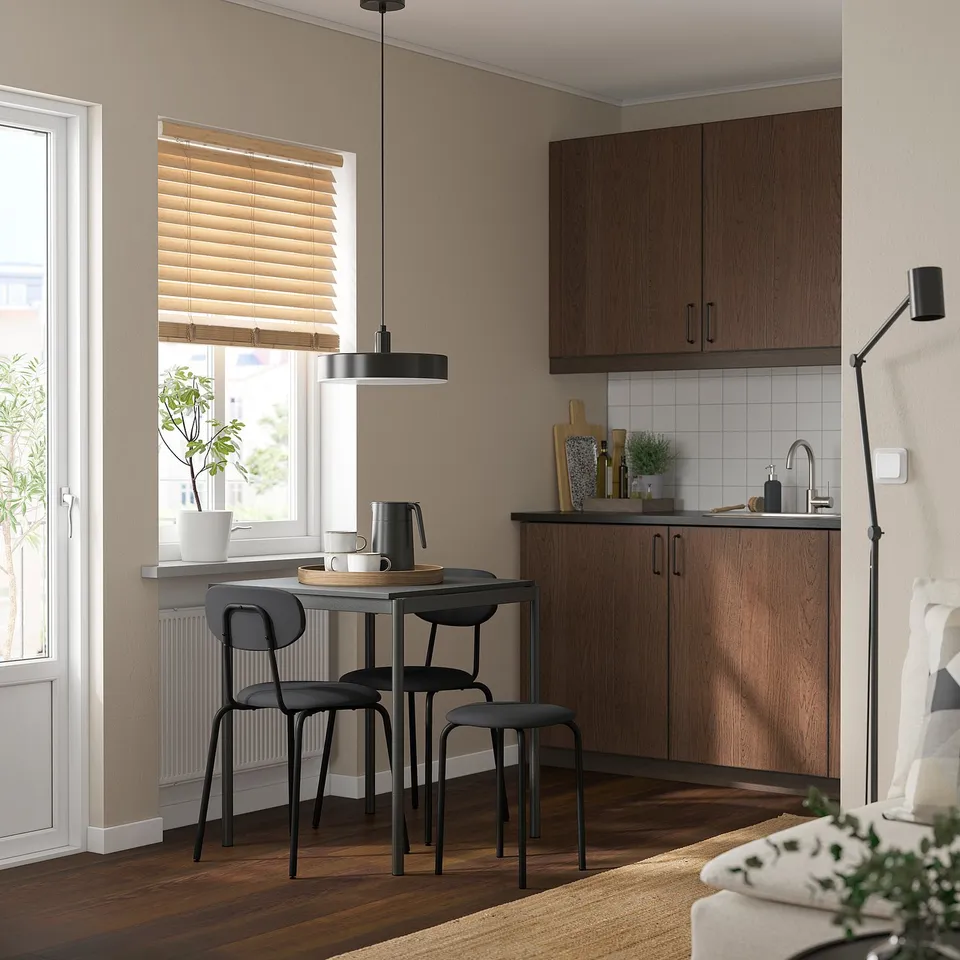 Small, modern kitchen with beige walls, wooden floors, and a GULTARP stool in black near a window. Wooden cabinets and modern decor.