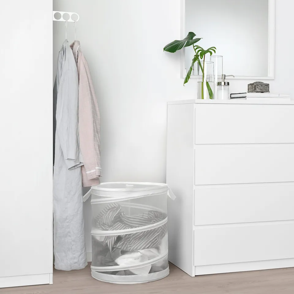 Minimalist bedroom: white basket with clothes, coat hanger, dresser with plant.