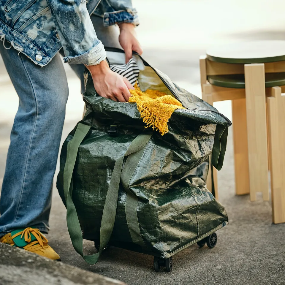 Person pulling large wheeled shopping bag with yellow handle.