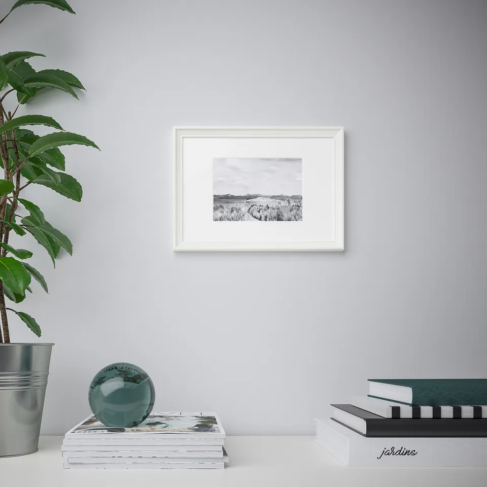 A minimalist living space with a framed black-and-white landscape on the wall, showcasing the decor versatility of the KNOPPÄNG picture frame.