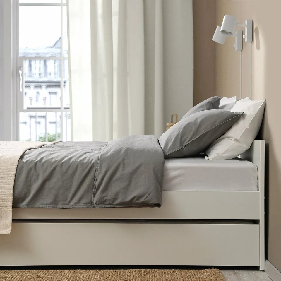Modern bed frame with a trundle and storage, featuring clean design and integrated storage boxes. The bed near a large window with curtains.