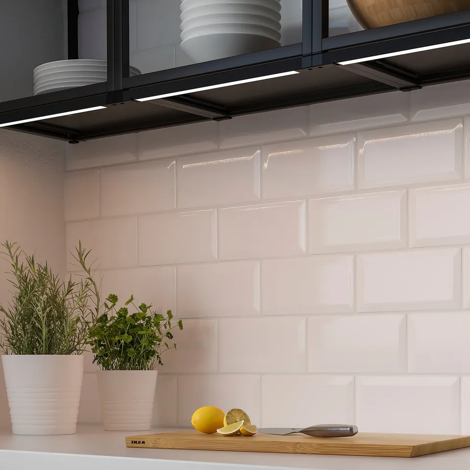 Kitchen counter with herbs, lemon, and a knife. Above, cabinet lighting with led strips, illuminating a white tiled backsplash.