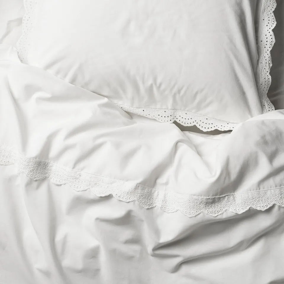 Crisp white bed linens with delicate lace trims, showcasing fine craftsmanship and soft fabric.