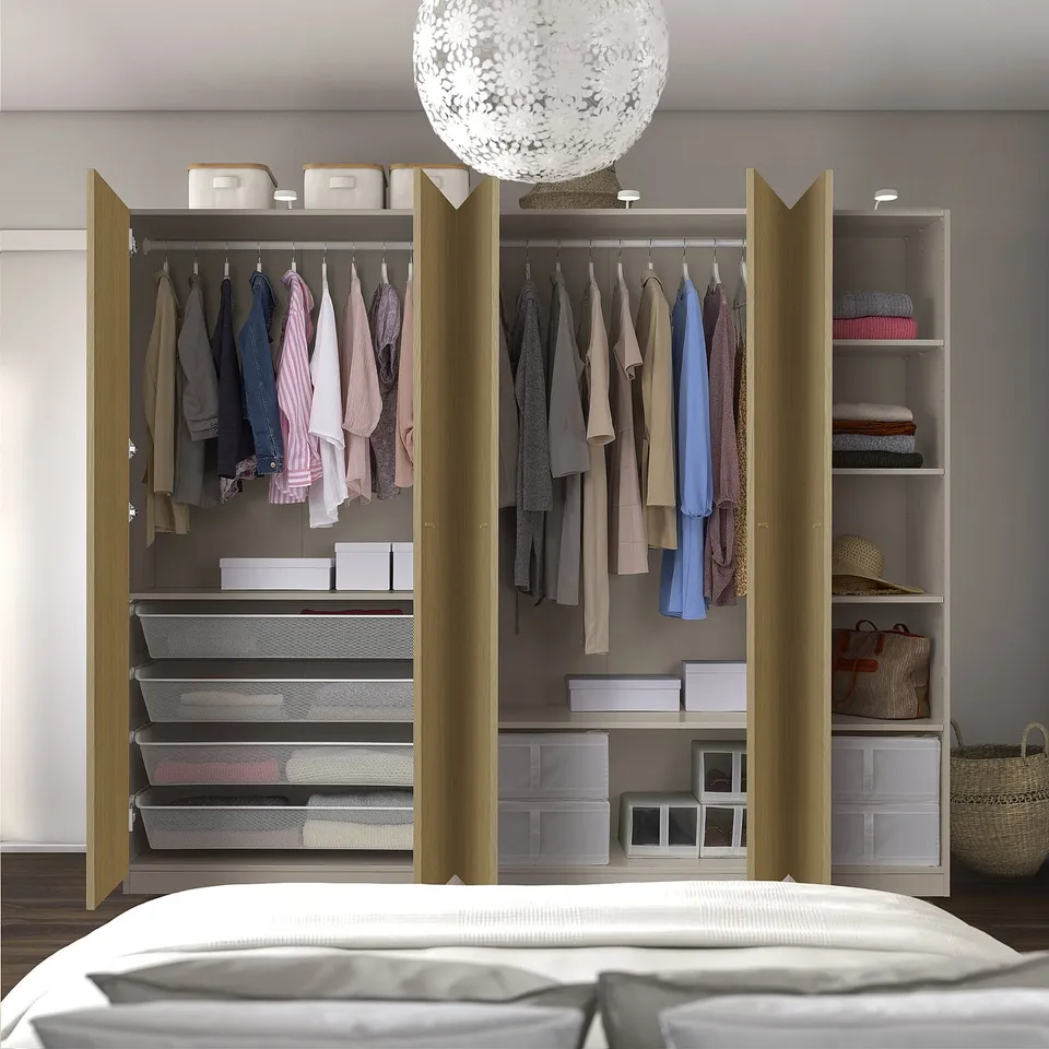 Modern bedroom with PAX wardrobe, open doors revealing clothes and storage, spherical light fixture. Partial bed visible.