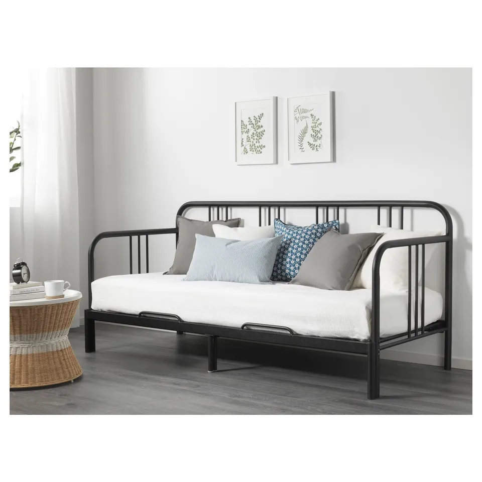 Daybed with metal frame, serving as a sofa with pillows, set against a wall with art prints.