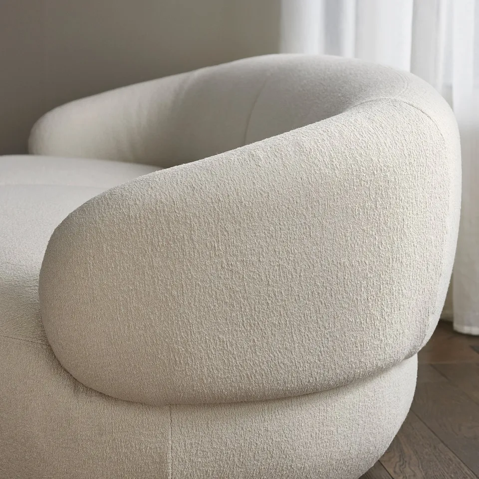 Modern, curved chair in soft cream fabric, plump cushions. Elegant and playful design.