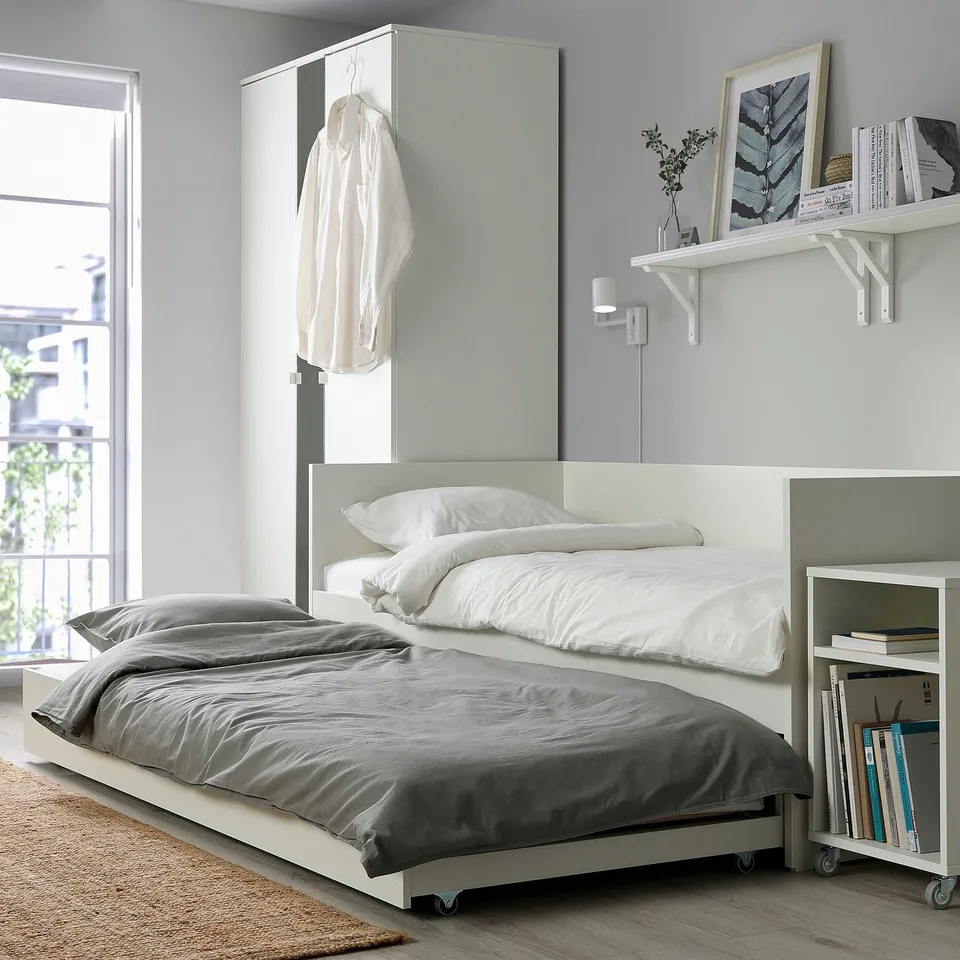 Modern daybed with trundle, white, grey bedding, wall-mounted bookshelf, hanging garments, minimalist decor.