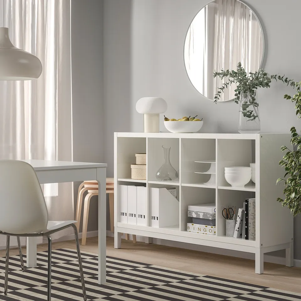 White KALLAX shelves with books, bowls, vases, and a lamp in a minimalist room.