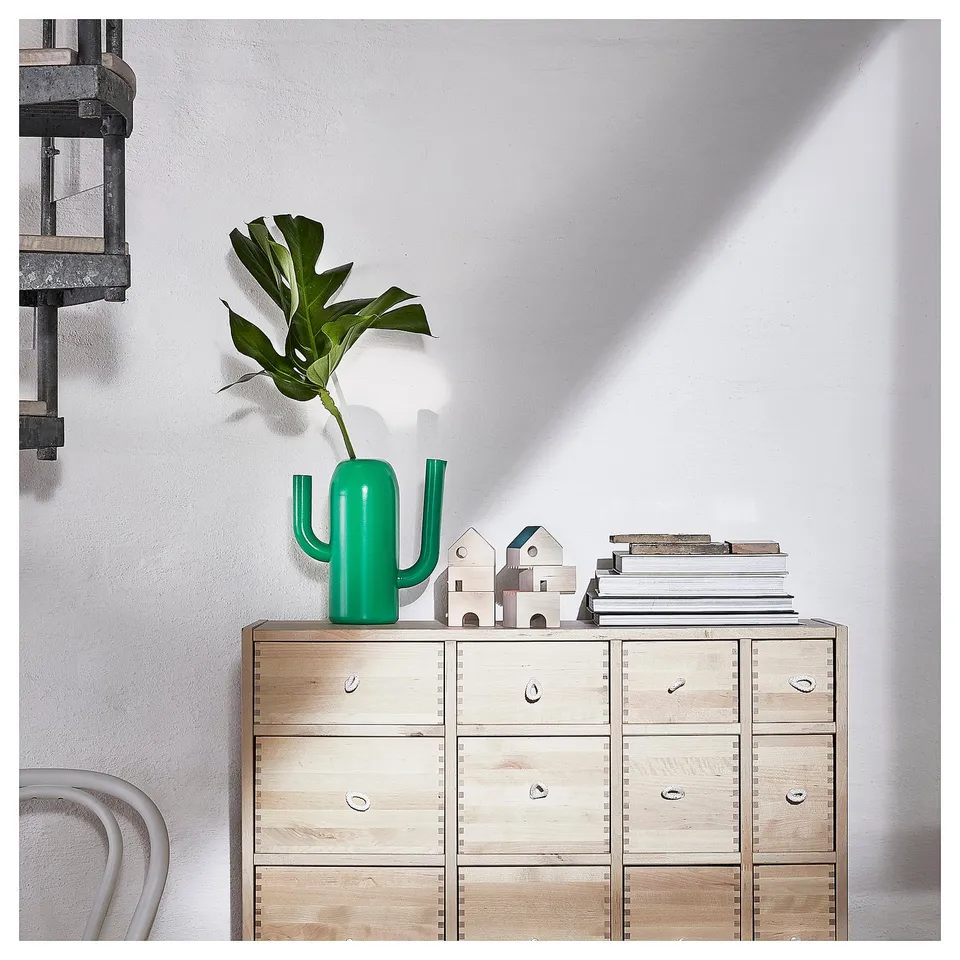 Bright green cactus-shaped vase on wooden dresser, surrounded by books and decorations.