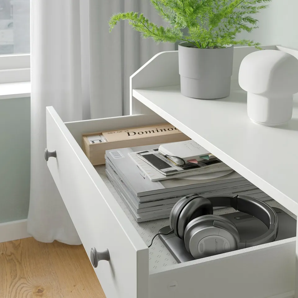 Modern white HAUGA drawer, open showing books, headphones, and home decor.