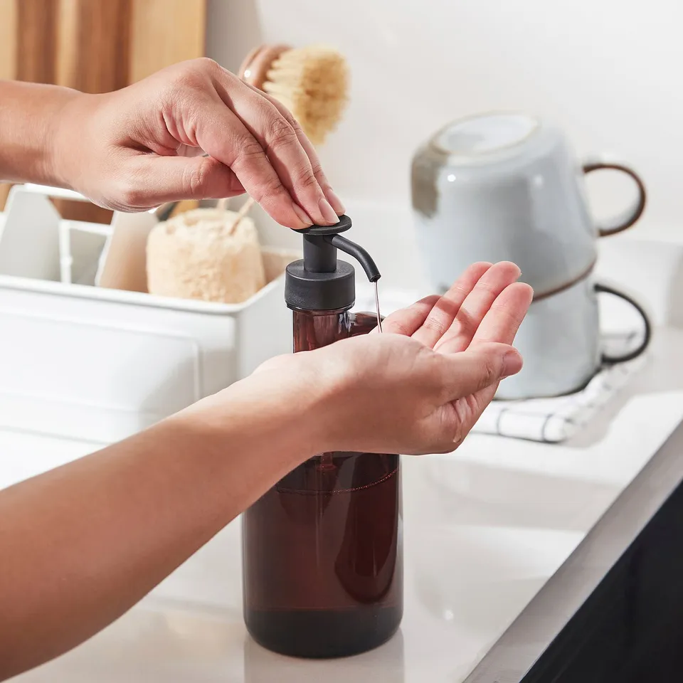 Person dispensing dark liquid from a soap dispenser onto their hand.