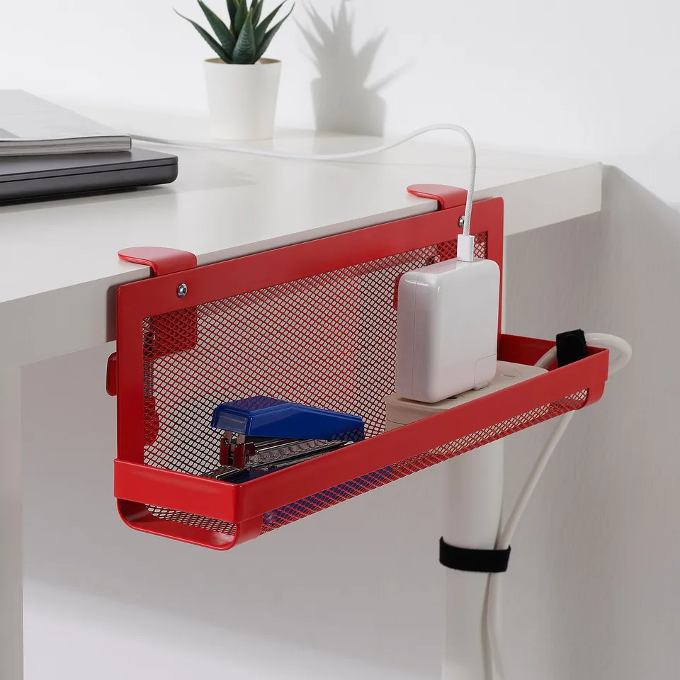 Red desk organiser with mesh, holding small office supplies and charging gadgets, mounted on a white desk.