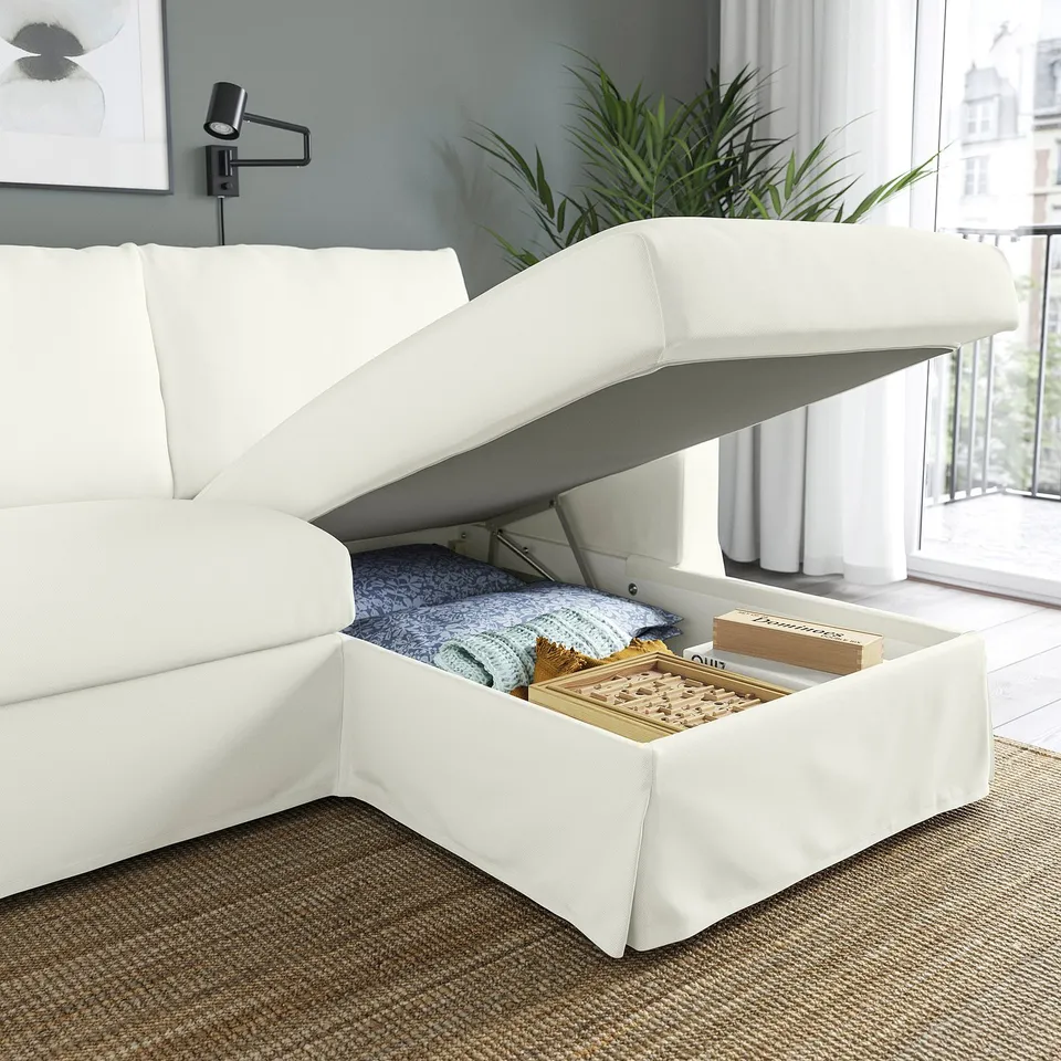 Modern white sofa with lift-up chaise longue revealing storage filled with blankets and games. Perfect for cosy living spaces.