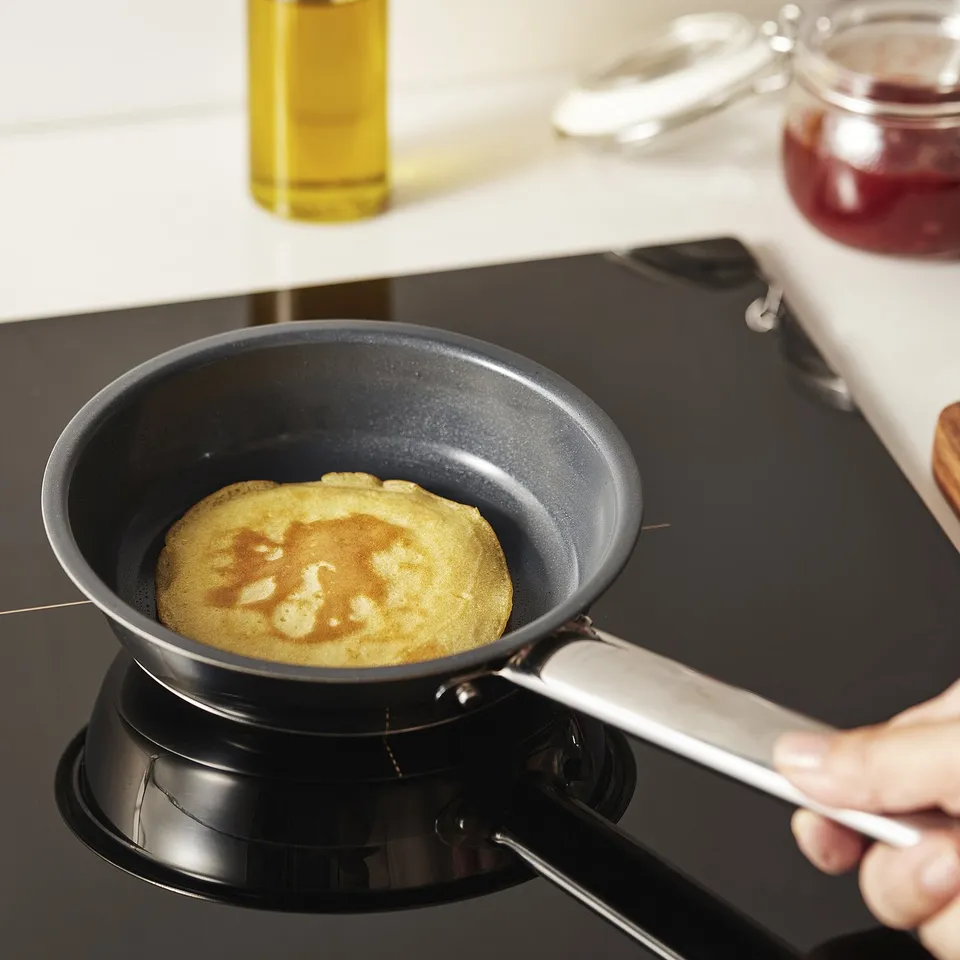Person cooking pancake in small, non-stick frying pan on stove.