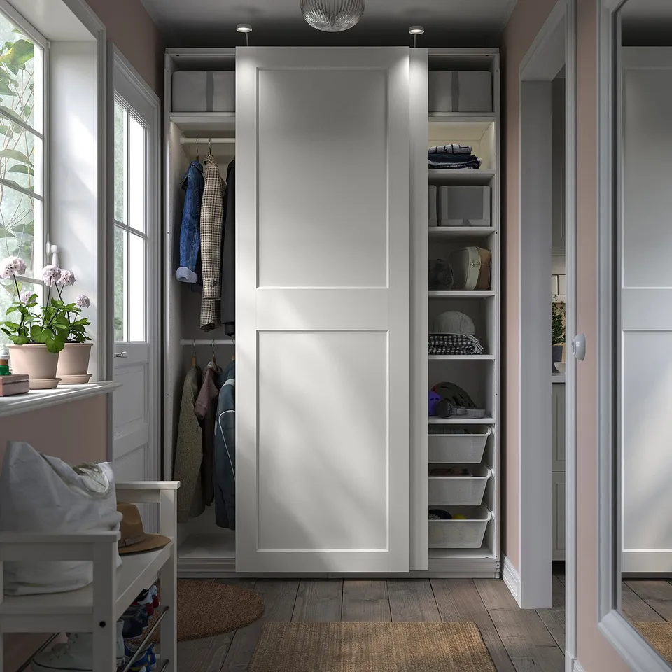 Modern white wardrobe with sliding doors, shelves, and hanging space. Includes a chair, plants, and wooden floor.