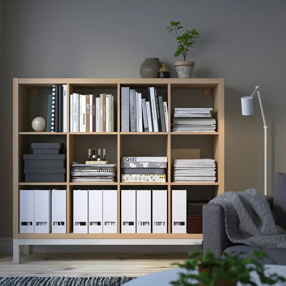 KALLAX shelving unit stores books, games, and decor. Tall, light wood, rectangular, with multiple compartments. Fits well in living spaces.