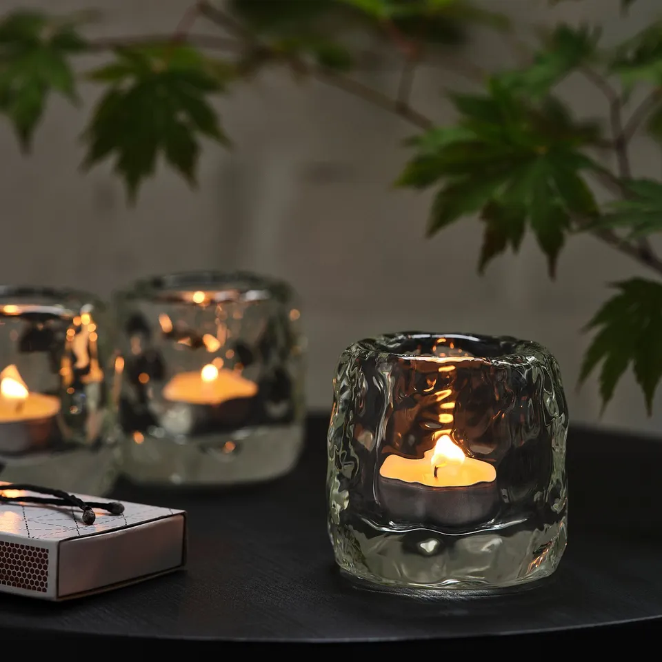 Tealight candles in textured glass, warm glow, matchbox, green leaves