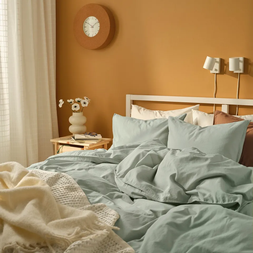 Mint green bedding, wall lamps, flowers, clock.