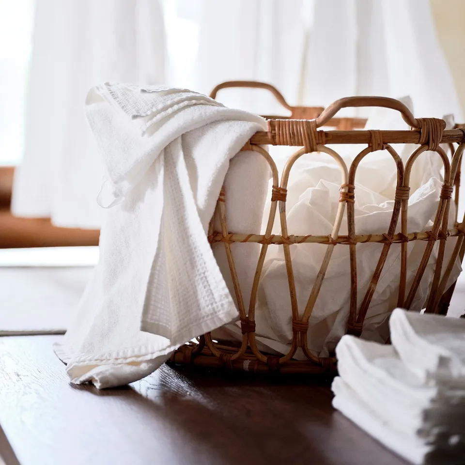 Wicker basket holding white towels on wooden table, perfect for bathroom or bedroom, showcasing its handcrafted, natural design.
