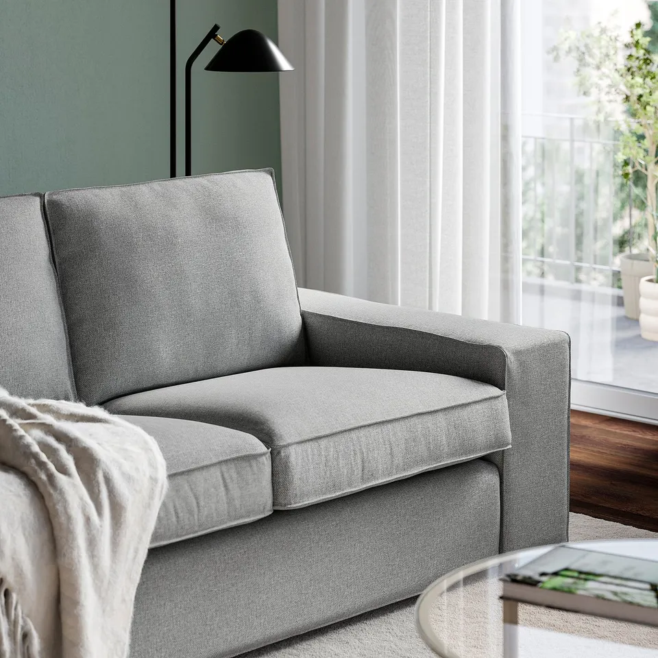 Grey sofa with cushions, wide armrests, near window.