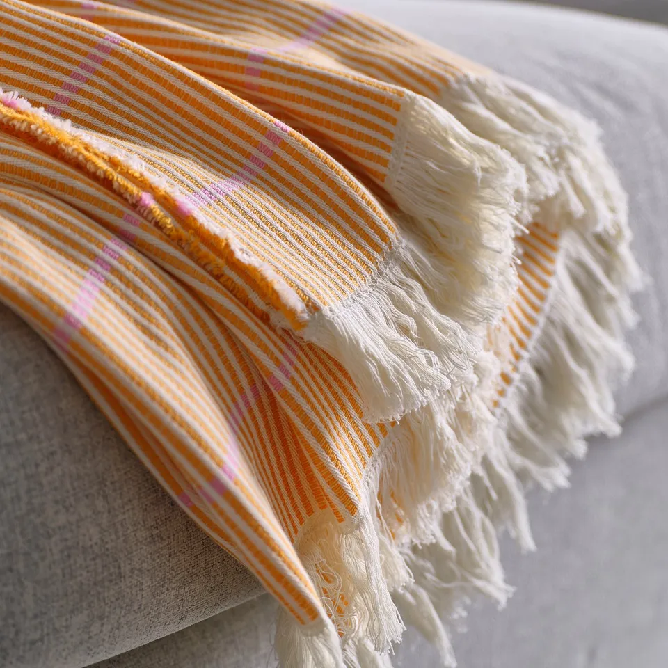 A bright orange throw with pink stripes and neatly frayed edges on a white surface.
