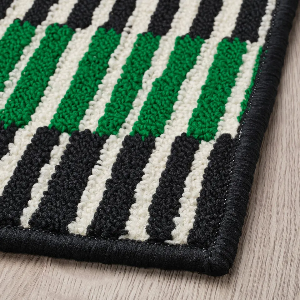 Striped door mat with black, white, and green patterns on a sturdy, non-slip rubber backing. High-quality, handcrafted design.