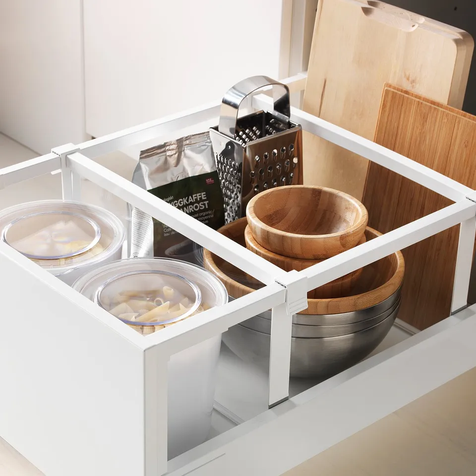 White kitchen drawer with glass bowls, wooden bowls, and graters in a well-organized storage system.
