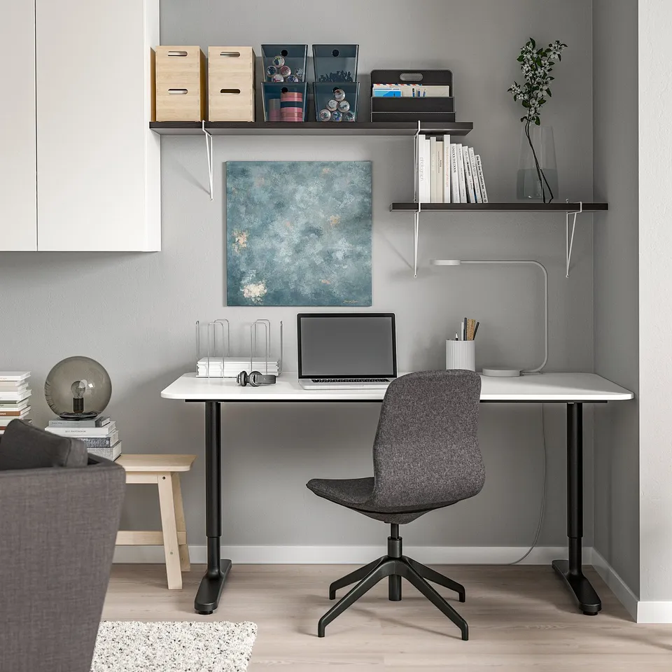 Modern home office with white desk, grey chair, shelves, and artwork.