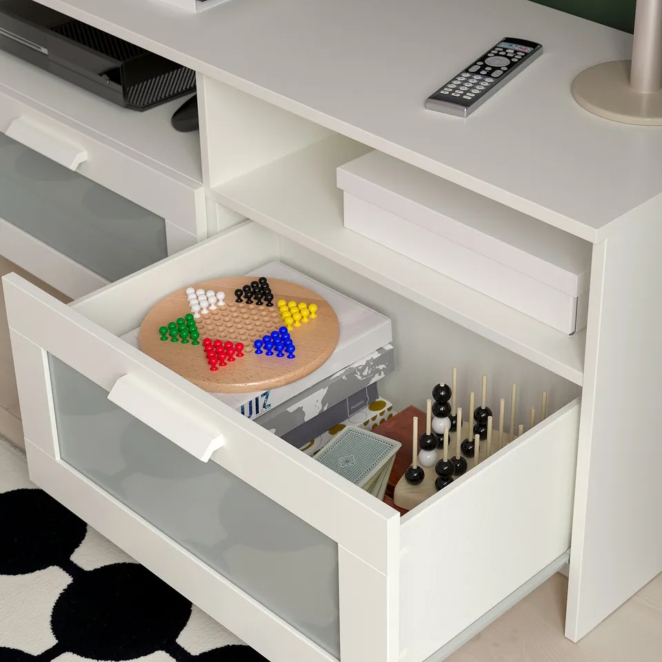 White tv stand with large drawers storing games and accessories. Cable management holes visible at back.