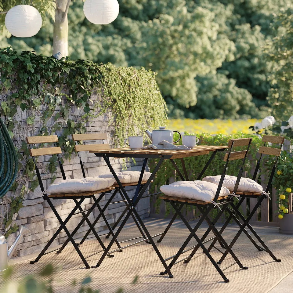 Small outdoor patio set in black and wood tones with cushions. Surrounded by greenery.