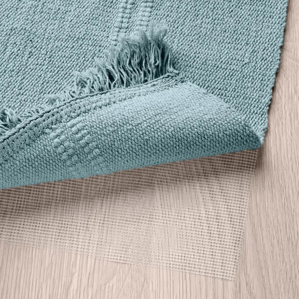 Light blue rug with fringes, shown on wooden floor.